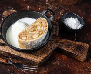 Apfelstrudel strudel with cinnamon, powdered sugar and vanilla ice cream in a pan. Dark background. Top view.